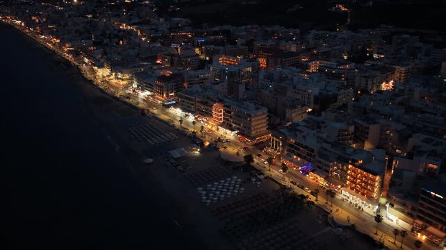 Aerial drone view of the sandy town beach and illuminated seafront hotels at night, Rethymno, Greece