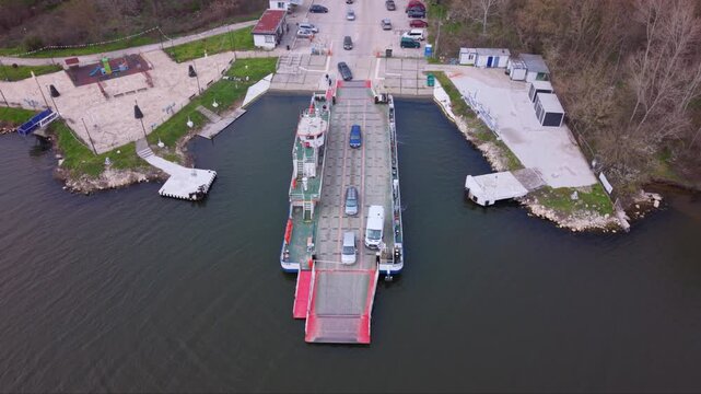 Aerial drone view of vehicle ferry transporting cars across a wide river with automobiles boarding and disembarking at ferry terminal connecting opposite riverbanks transportation infrastructure RO-RO