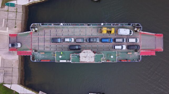 Aerial drone view of vehicle ferry transporting cars across a wide river with automobiles boarding and disembarking at ferry terminal connecting opposite riverbanks transportation infrastructure RO-RO