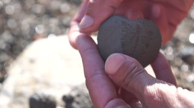 Clay imprint hands outdoors, person showing natural leaf pattern on sunny day, creative nature craft activity