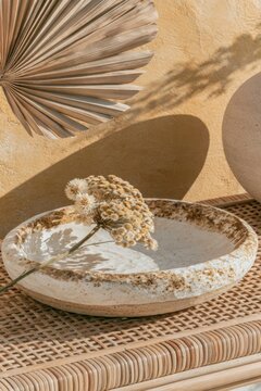 Closeup of hand-thrown ceramic key dish with dried flowers placed on a woven surface, featuring a decorative fan and a round vase in a warm-toned setting
