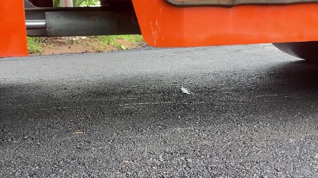 Truck exhaust pipe: This close-up shot shows a section of an orange truck with a metal exhaust pipe. The exhaust pipe is positioned above the asphalt road, suggesting it's on a street or parking lot.