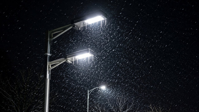 Snowfall and icicles illuminated by modern LED street lights on a cold winter night