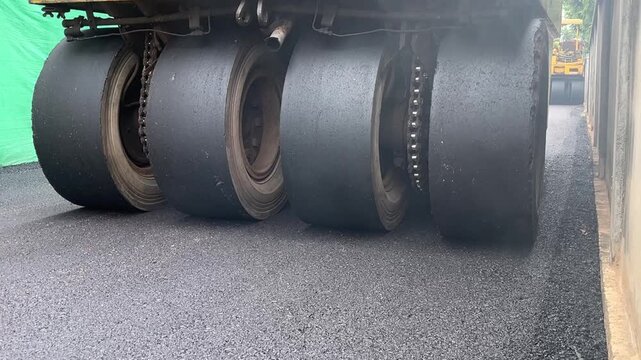 Heavy Machinery Compacting Asphalt: The large, heavy tires of a road roller press down on freshly laid asphalt, smoothing the surface for road construction.