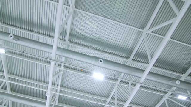 Industrial ceiling features large metal ventilation pipe trusses and lamps. Professional installation ensures constant air flow in facility