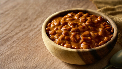 homemade cowboy meal or pinto bean in a wooden bowl on a table. Savory stewed baked bean with rich sauce, perfect for a hearty meal, breakfast, barbecue, background with copy space © boommaval