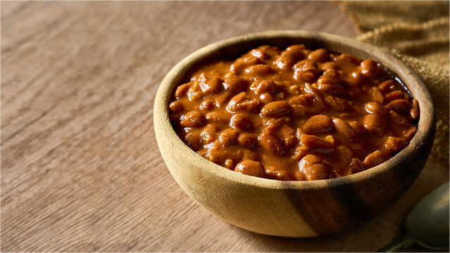 homemade cowboy meal or pinto bean in a wooden bowl on a table. Savory stewed baked bean with rich sauce, perfect for a hearty meal, breakfast, barbecue, background with copy space