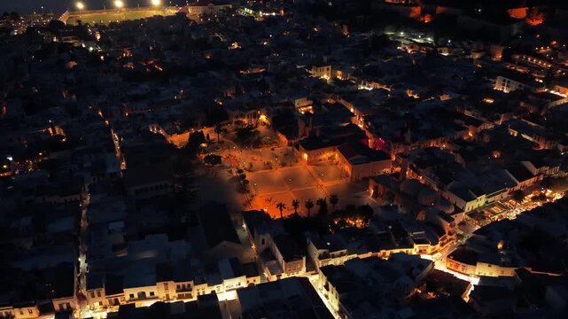 Aerial drone view of the illuminated old town square and the Neratze Mosque domes glowing at night, Rethymno, Greece