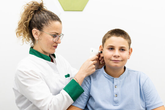 Female pediatrician performing an ear examination with an otoscope on a young boy during a routine medical checkup in a modern healthcare clinic.