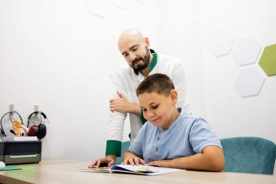 An ear, nose, and throat doctor reads a book to a child between 10 and 12 years old during a pediatric consultation at a modern medical clinic.