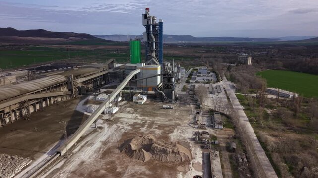 High-resolution aerial footage of a modern cement manufacturing plant surrounded by limestone quarries, industrial infrastructure, railway sidings, and agricultural fields in Bulgaria. Ideal for illus