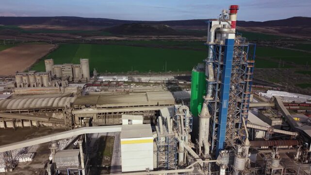 High-resolution aerial footage of a modern cement manufacturing plant surrounded by limestone quarries, industrial infrastructure, railway sidings, and agricultural fields in Bulgaria. Ideal for illus
