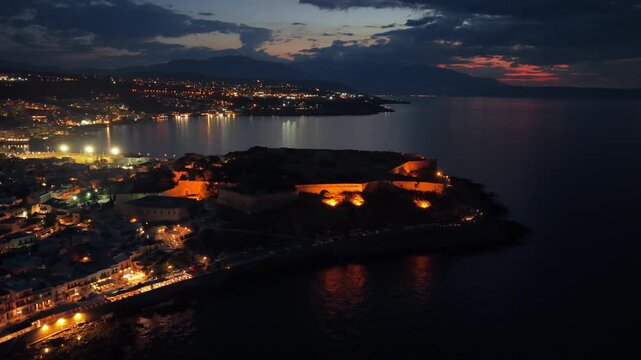 Aerial drone view of the Venetian Fortezza with floodlit walls on its headland above the sea, Rethymno, Greece