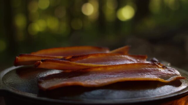 Close low-angle view of bacon strips sizzling in hot cast-iron pan, with rising steam, curling edges, rendered fat, and deepening golden browning, with bacon, pork, meat, pan detail