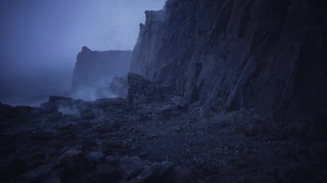 foggy rocky coastline at dawn, low visibility over pebble slope and fractured cliff faces, pale blue light and muted tones suggest calm yet eerie atmosphere