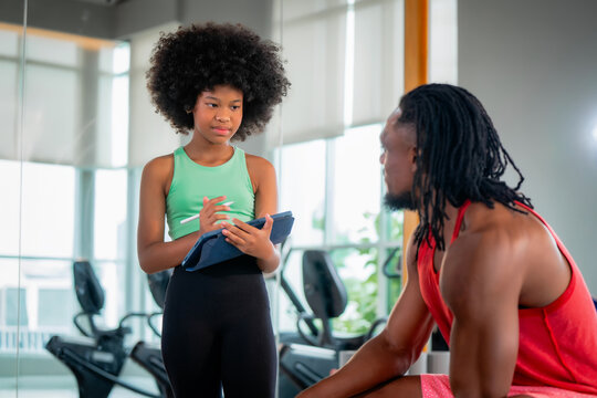 African American girl holding tablet talking to father coach gym. Concept of family fitness, healthy active lifestyle, digital workout tracking and strong family bonding.