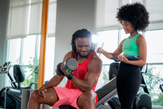 Fit African father lifting weight young daughter digital tracking tablet. Scene for family exercise motivation, fitness tracking application, quality time and body positivity.