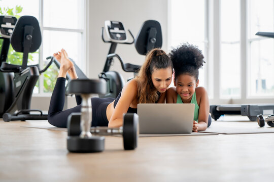 Fitness coach mother checking digital workout plan online with daughter. Scene for personal coaching session, online fitness education, tech in sports and family wellness.