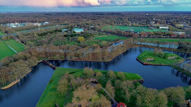 Aerial wide angle panoramic view of historic star fortress green earthwork bastions with old stone bunkers and defensive moats under a dramatic evening sunset sky