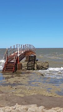 Abandoned and rusty footbridge on the rocky coast with crashing ocean waves