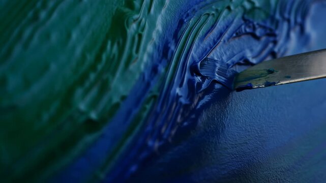 Palette knife spreading thick cobalt and teal paint across textured surface, forming glossy ridges, smooth swaths, curved strokes, and rich mixed pigment detail