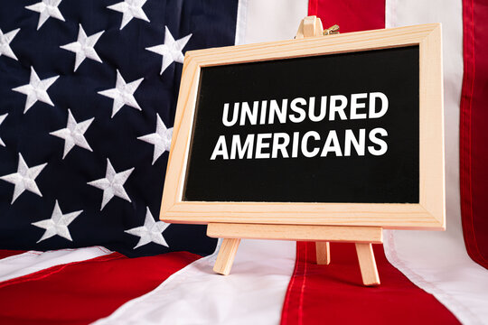 Uninsured Americans text on black chalkboard with wooden easel on USA flag background, healthcare policy and social concept