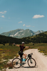 Fototapeta premium Happy woman posing with outstretched arms on a gravel bicycle in Durmitor National Park, Montenegro. Summer bikepacking adventure in alpine mountains.