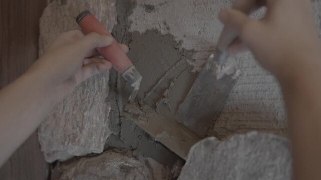 First-person point-of-view shot of a professional worker applying a smooth layer of gray cement mortar onto a wall surface during home renovation. Close up, macro detail of the tool texture and motion
