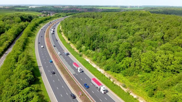 Aerial drone footage above a busy UK motorway following traffic with vehicles speeding long distance through woodland and countryside