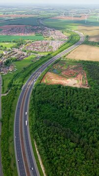 Aerial vertical landscape footage of a major motorway in the UK winding its way through countryside into the distance with traffic and copy space