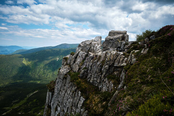 Fototapeta premium A wide horizontal shot of rugged, weathered grey boulders and rock crags towering on a high alpine summit under a cloudy sky, perfect for geology education and outdoor adventure marketing.