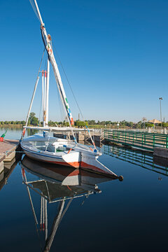 Traditional Egyptian sailing felluca river boat moored on the Nile bank at small jetty with reflection in water