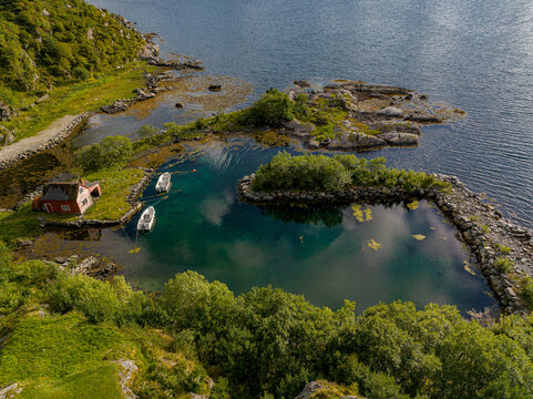 Aerial view of traditional red house and boats in a turquoise emerald water lagoon near Maloy Bridge, Norway