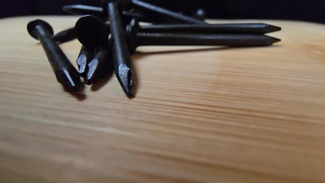 Close-up of black iron nails arranged on a clean wooden surface. High-quality macro shot showcasing construction materials and hardware tools for DIY, carpentry, or industrial renovation projects.