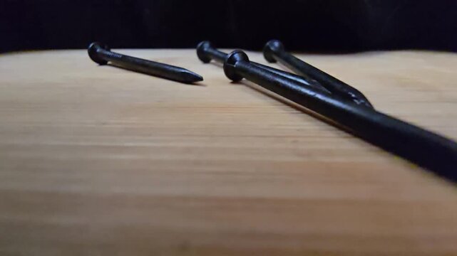 Close-up of black iron nails arranged on a clean wooden surface. High-quality macro shot showcasing construction materials and hardware tools for DIY, carpentry, or industrial renovation projects.