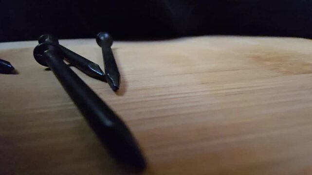 Close-up of black iron nails arranged on a clean wooden surface. High-quality macro shot showcasing construction materials and hardware tools for DIY, carpentry, or industrial renovation projects.