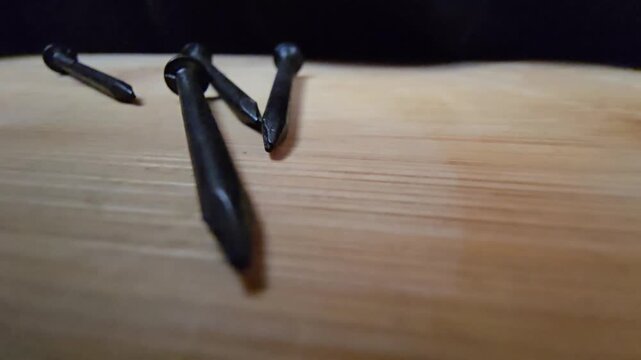 Close-up of black iron nails arranged on a clean wooden surface. High-quality macro shot showcasing construction materials and hardware tools for DIY, carpentry, or industrial renovation projects.