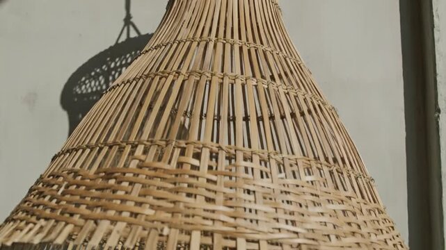 A video showcasing a woven bamboo lamp hanging against a wall, capturing the intricate textures and the dynamic interplay of sunlight and shadows as the camera angles change.