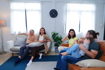 Fototapeta premium The son, parents, and grandparents sit on the sofa watching TV, cheering on their favorite team, enjoying themselves together in the living room of their home. A family and three-generational concept.