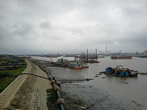 Industrial sand dredging boats and pipelines working on a river bank under a cloudy sky