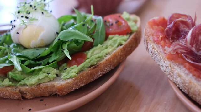 Close-up of traditional breakfast sandwiches at a local caf&eacute; in Santander, Cantabria. Spanish pan con tomate with jam&oacute;n and a boiled egg with avocado, tomatoes, and arugula. Shallow depth of field.
