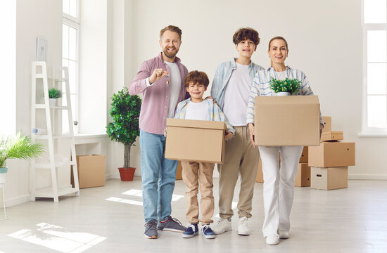 Happy young family with two kids on moving day smiling with unpacked boxes in hands in their new apartment. Home owners enjoying buying flat. Relocating, real estate, mortgage concept.