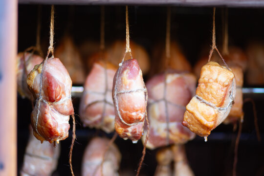 Several smoked meat pieces hanging in a dark curing room, artisanal food production, rustic cooking, traditional preserved delicacy.