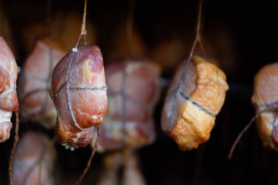 Smoked meat pieces hanging on strings in a dark curing area, traditional food preparation, rustic delicacy, artisanal cooking, preserved meat.
