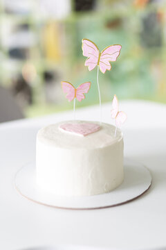 White cake with pink heart and butterfly toppers on a plate, sweet celebration dessert, romantic party decor, pastel festive mood.