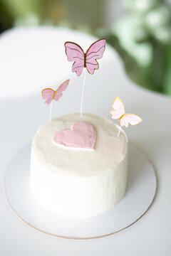 White mini cake with pink heart and butterfly toppers on a plate, elegant dessert, pastel party styling, romantic festive celebration.