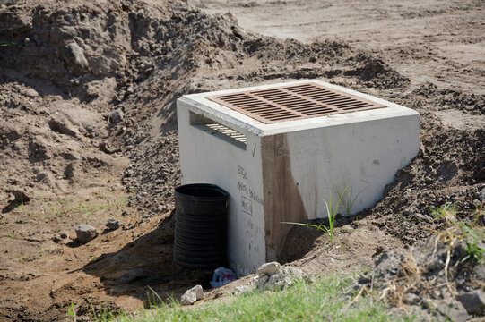 Storm drainage culvert with a metal grate sits partially buried at a construction site, surrounded by excavated soil and sparse grass, illustrating infrastructure, erosion control, and stormwater mana