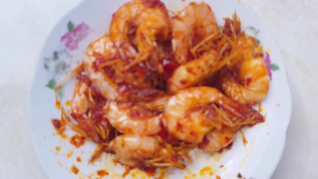 Close-up footage of spicy fried shrimp with red chili paste (udang balado) served on a floral plate, showcasing glossy texture and authentic Indonesian home cooking