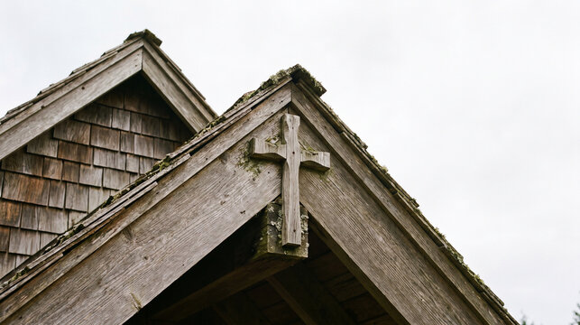 Closeup of a weathered wooden church roof with a carved cross detail against a bright sky
