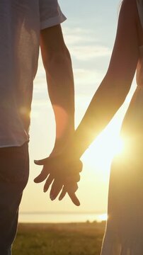 Silhouette of a young couple in love tenderly joining hands while standing together in a field at sunset, expressing romance, care, and a strong relationship during a beautiful golden hour